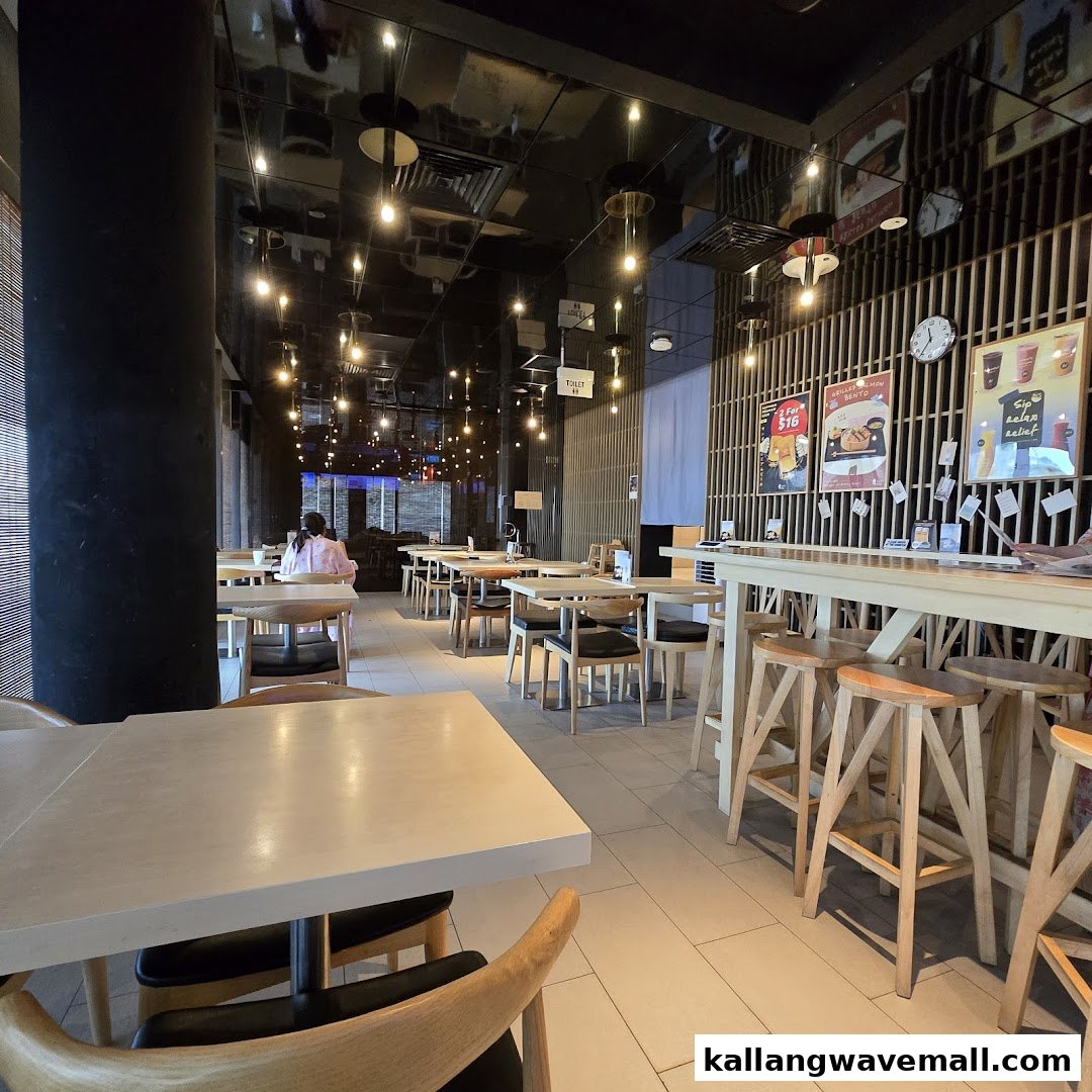 A spacious dining area with wooden tables, chairs, and warm overhead lighting, featuring a customer seated in the background.