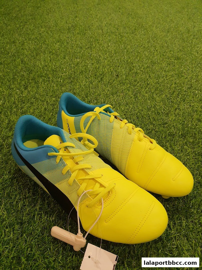 A pair of bright yellow and blue soccer cleats with laces on a green grassy surface.