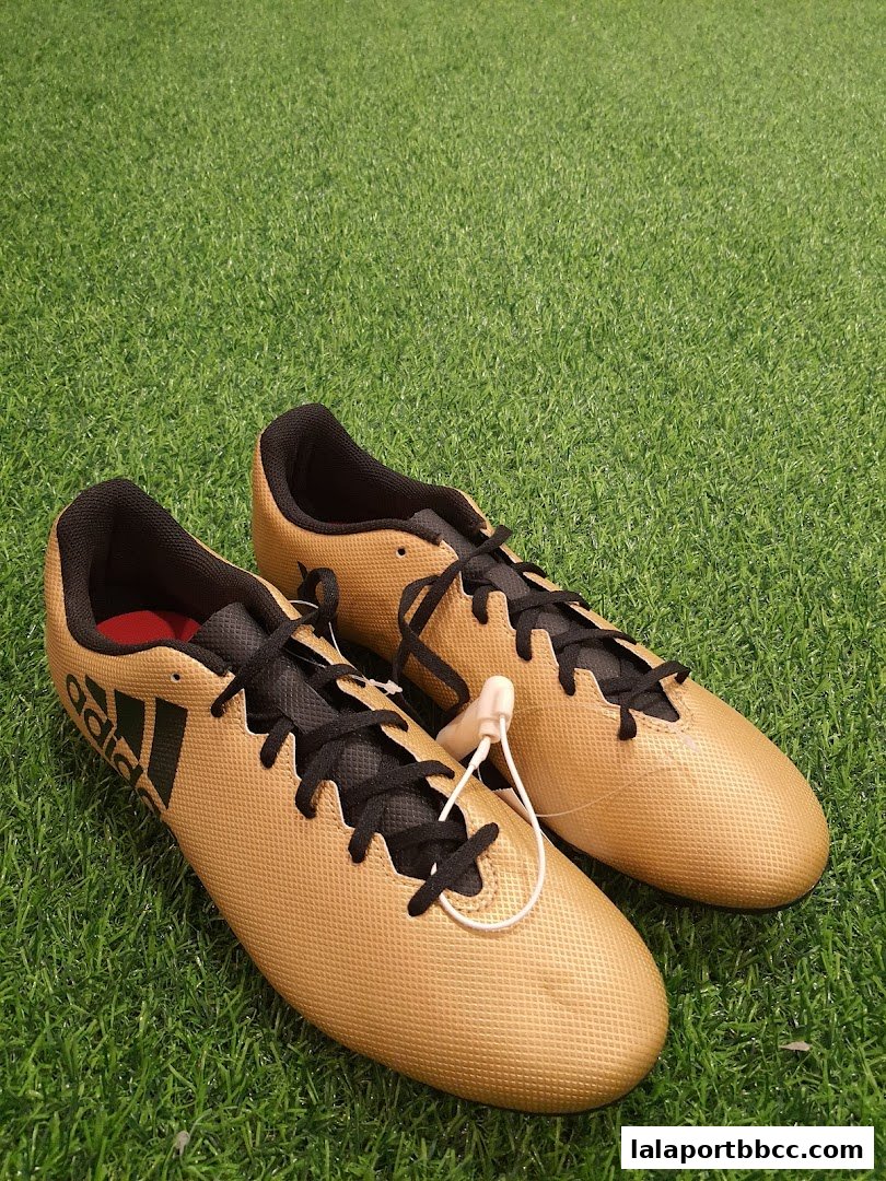 A pair of gold Adidas soccer cleats with black laces and accents on a green grassy surface.