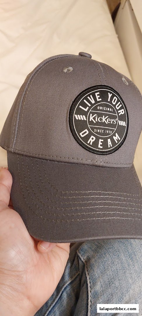 A person holds a grey Kickers baseball cap with a circular logo.