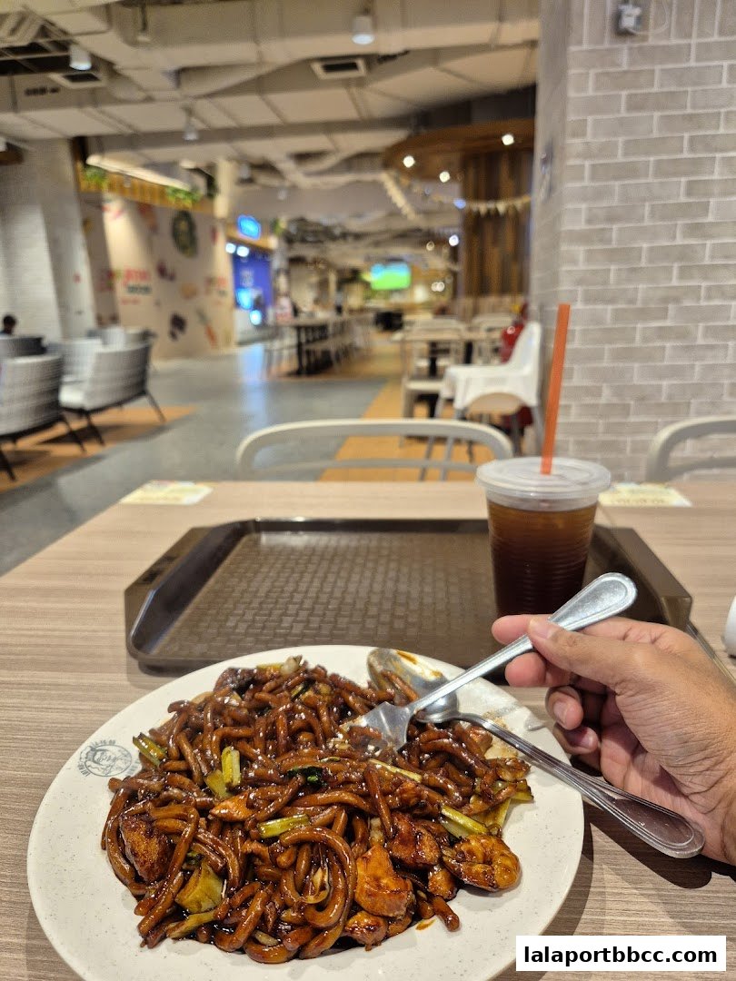 A plate of Hokkien Mee with a drink, ready to be eaten at a food court.