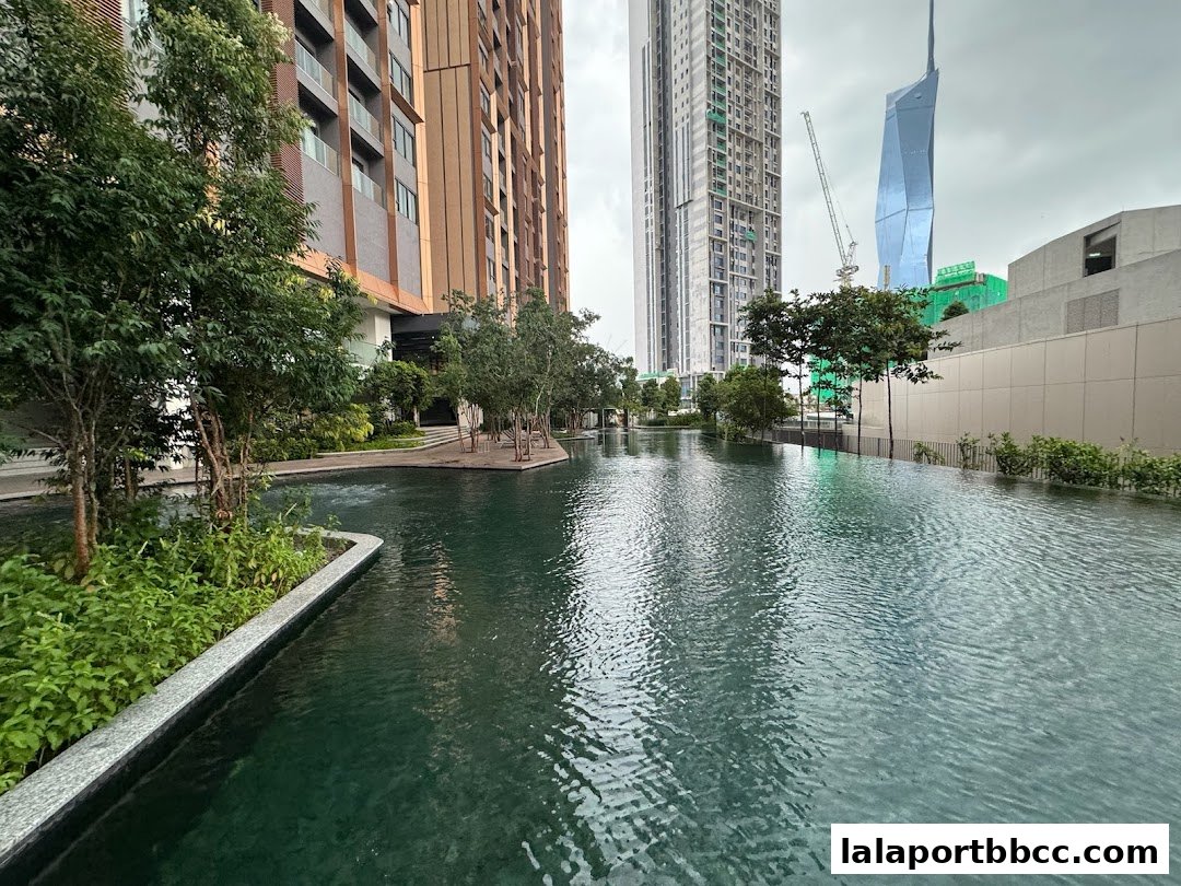 A serene water feature with lush greenery and modern buildings in the background.