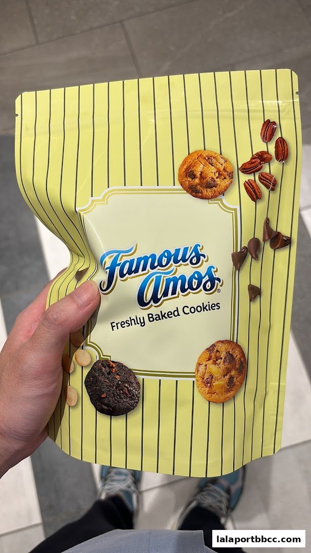 A hand holds a bag of Famous Amos freshly baked cookies with images of cookies and ingredients.