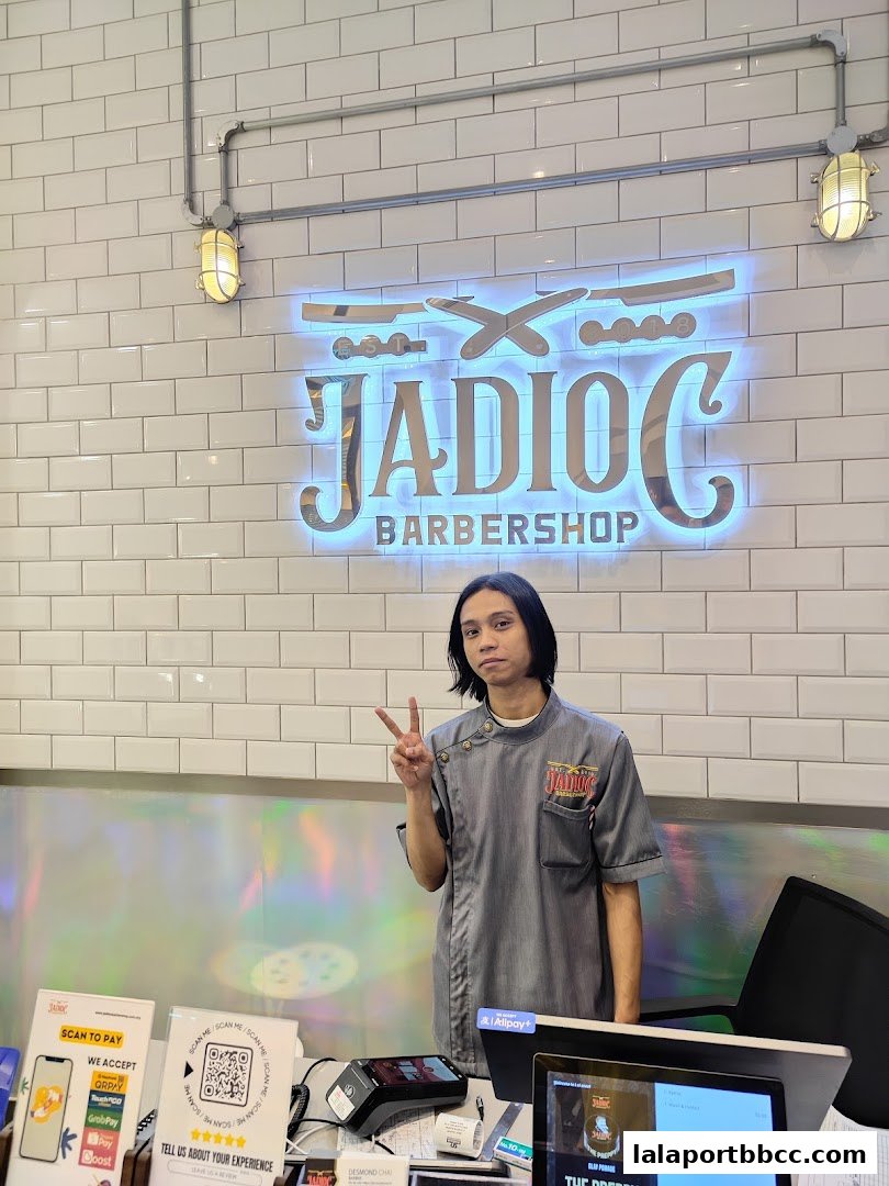 A barber stands in front of the Jadioc Barbershop sign, giving a peace sign.