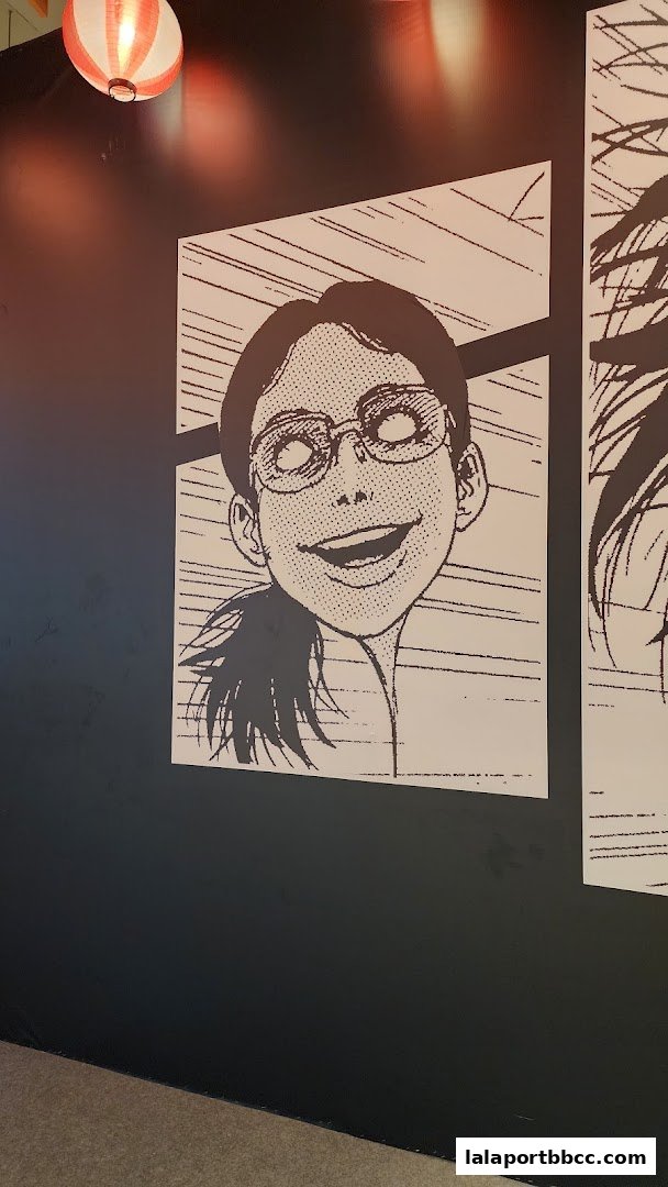 A black and white manga-style illustration of a smiling woman with glasses on a dark wall.