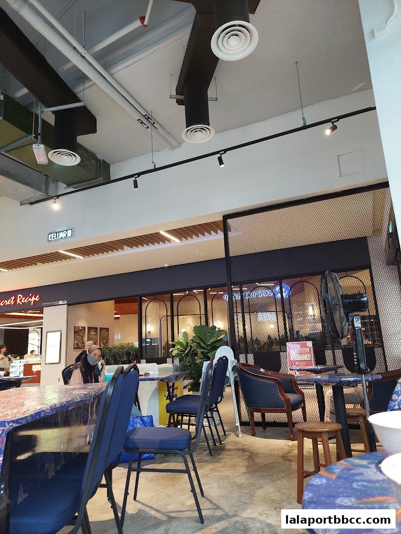 Interior view of a restaurant with tables, chairs, and plants, showing a glimpse of another shop.