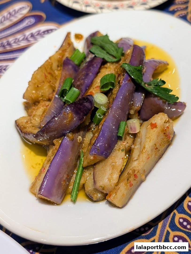A plate of stir-fried eggplant with scallions and a savory sauce.