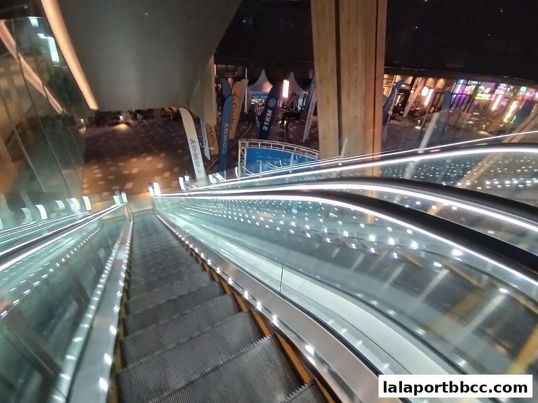 View from an escalator looking down towards a mall concourse with various booths and displays.