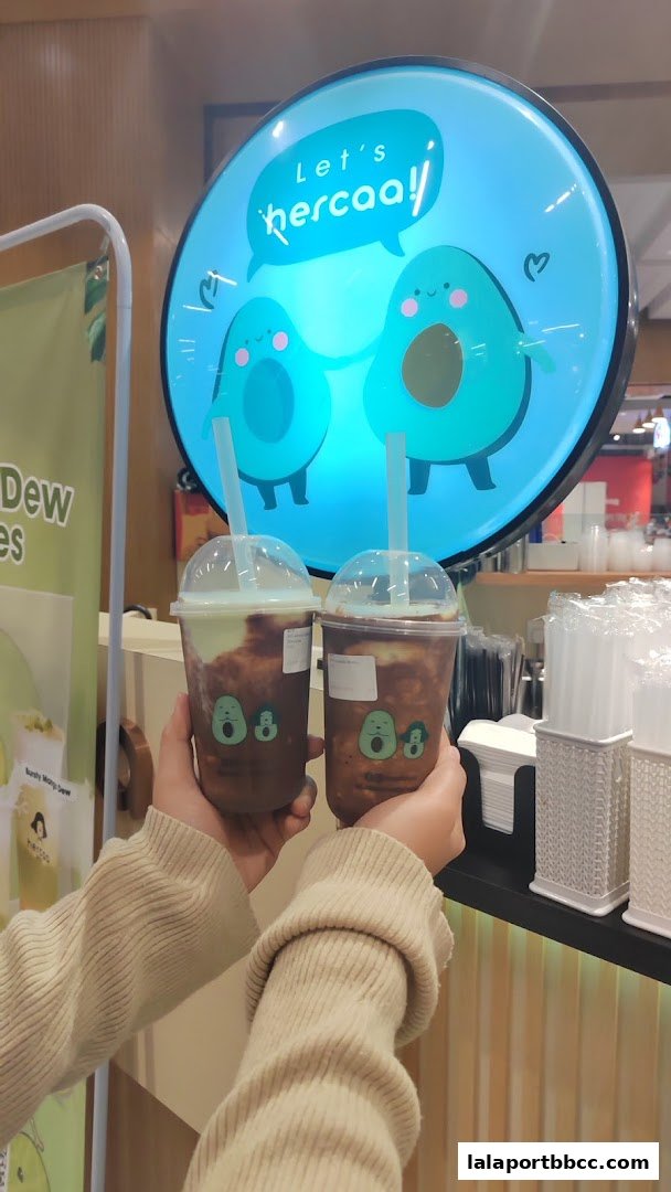 Two people holding refreshing drinks with the Hercaa logo and cute avocado characters.