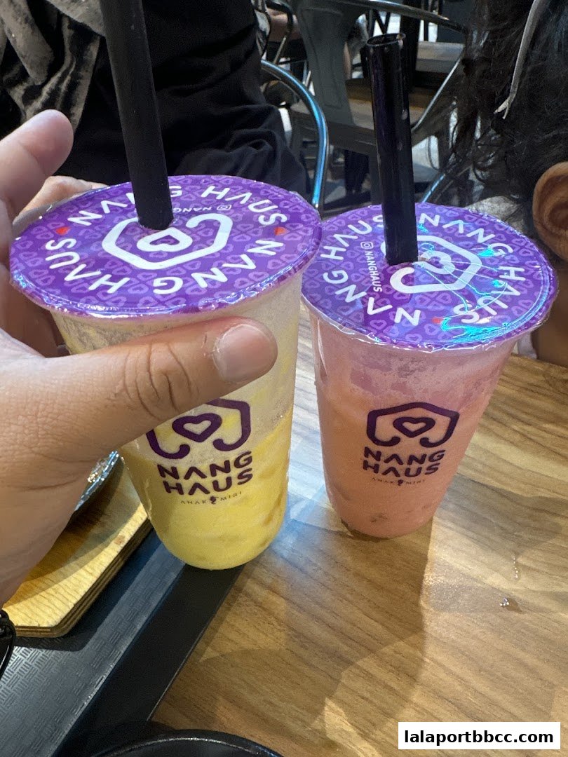 Two refreshing drinks from Nang Haus, one yellow and one pink, with branded purple lids.