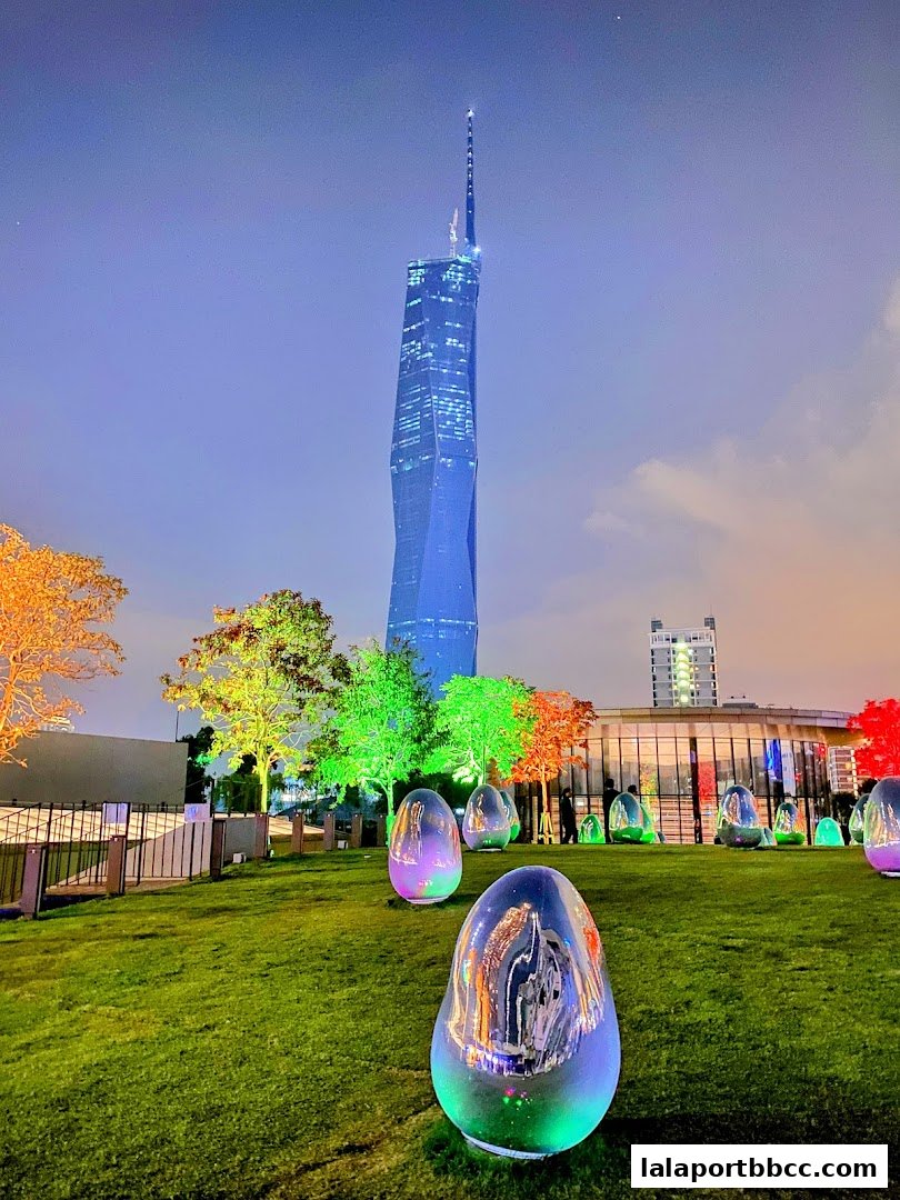 A nighttime view of a park with illuminated egg-shaped sculptures and a tall skyscraper in the background.