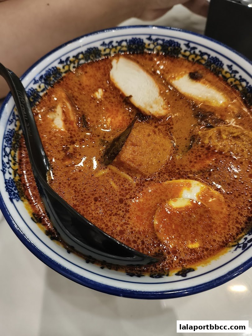 A close-up shot of a steaming bowl of curry laksa with chicken, egg, and tofu.
