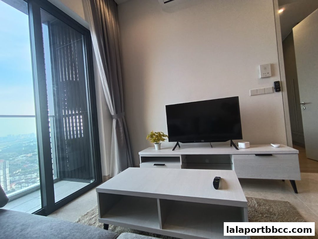 A modern living room with a TV, coffee table, and a large window overlooking a city.