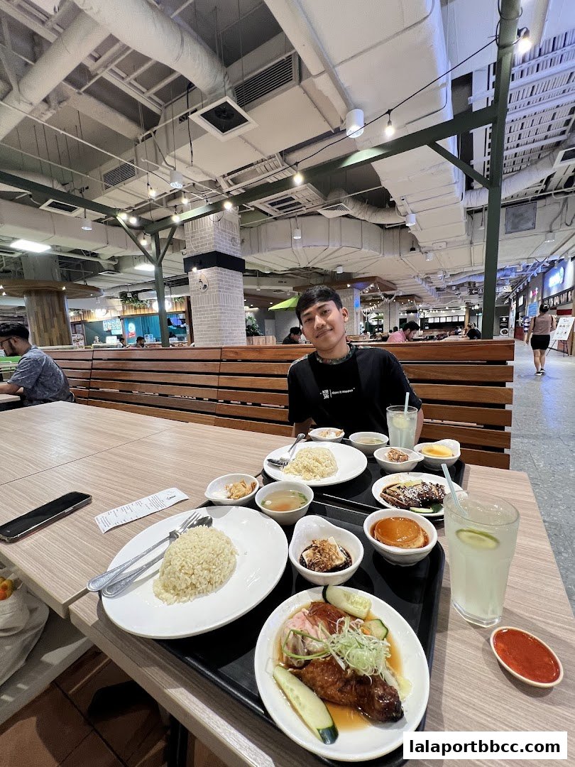 A person sits at a table with a meal of chicken rice, soup, and drinks.