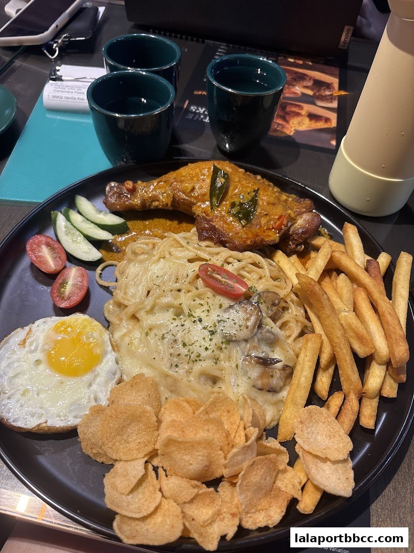 A plate of food featuring chicken, pasta, fries, a fried egg, and crackers, with drinks in the background.