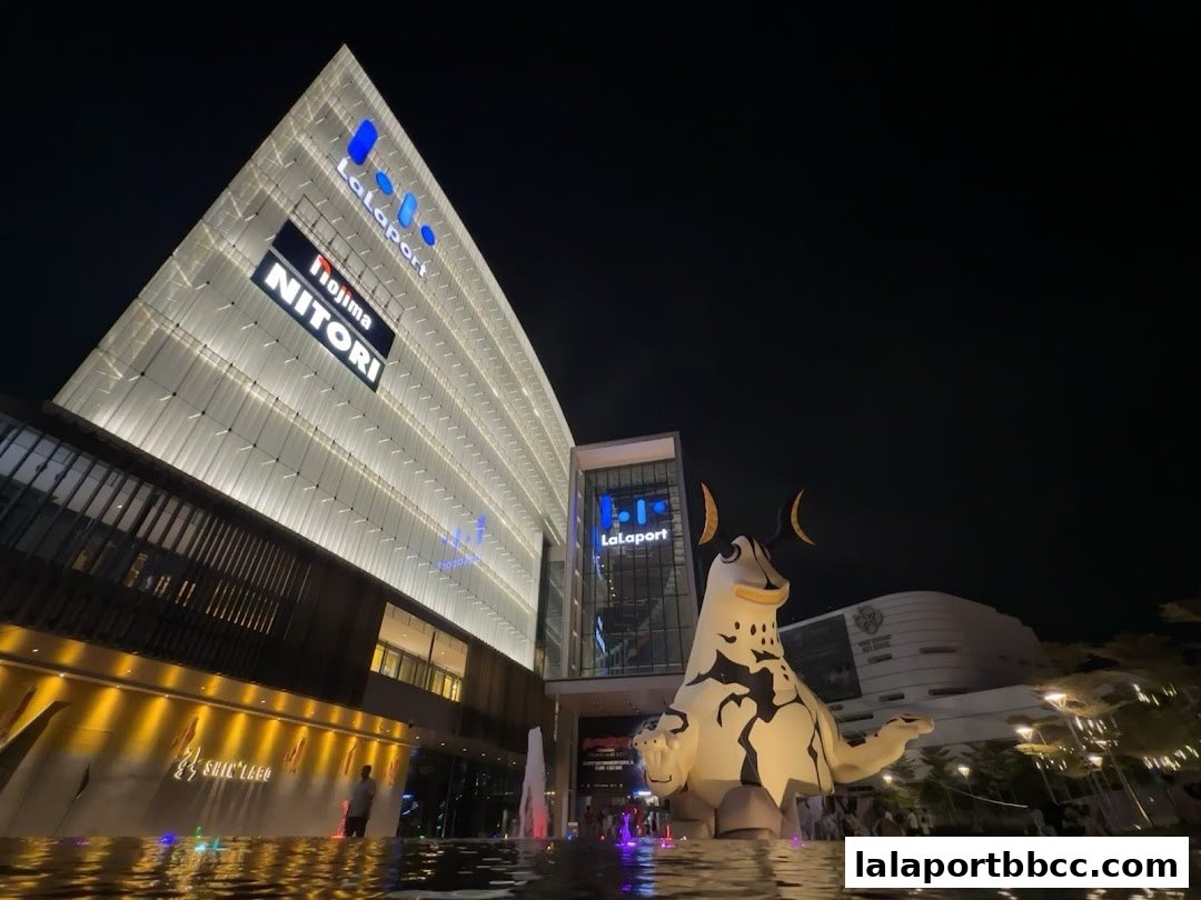 A large, illuminated shopping mall with a prominent mascot statue at night.