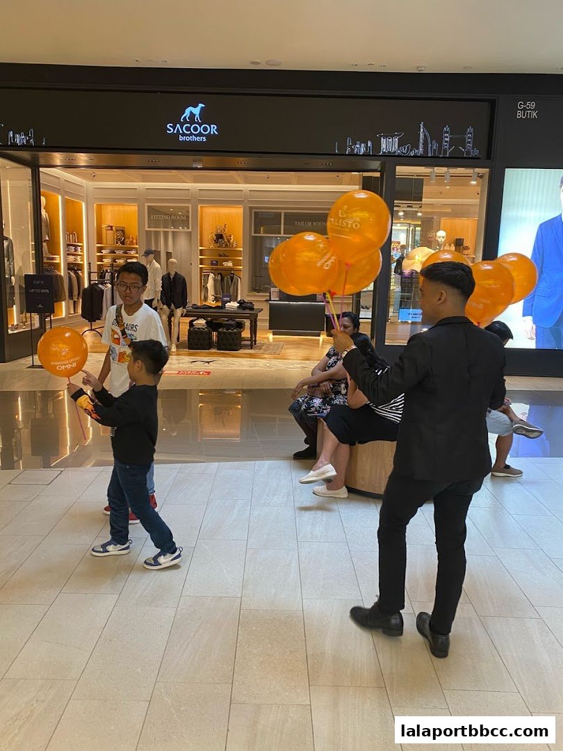 A man hands out orange balloons in front of a Sacoor Brothers store.