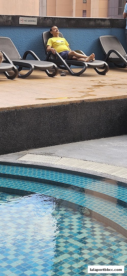 A man relaxes on a lounge chair by a swimming pool with blue tiled steps.