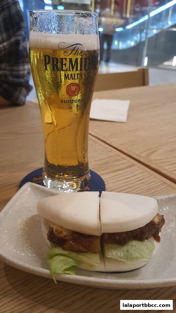 A glass of premium beer sits next to a delicious bao bun on a wooden table.
