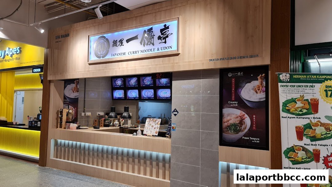 A food stall offering Japanese curry noodles and udon, with digital menus and promotional posters.
