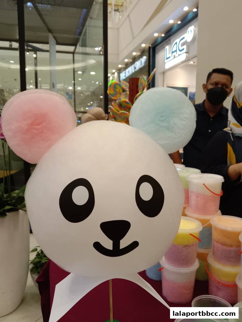A cute panda-shaped cotton candy with colorful cotton candy tubs in the background.