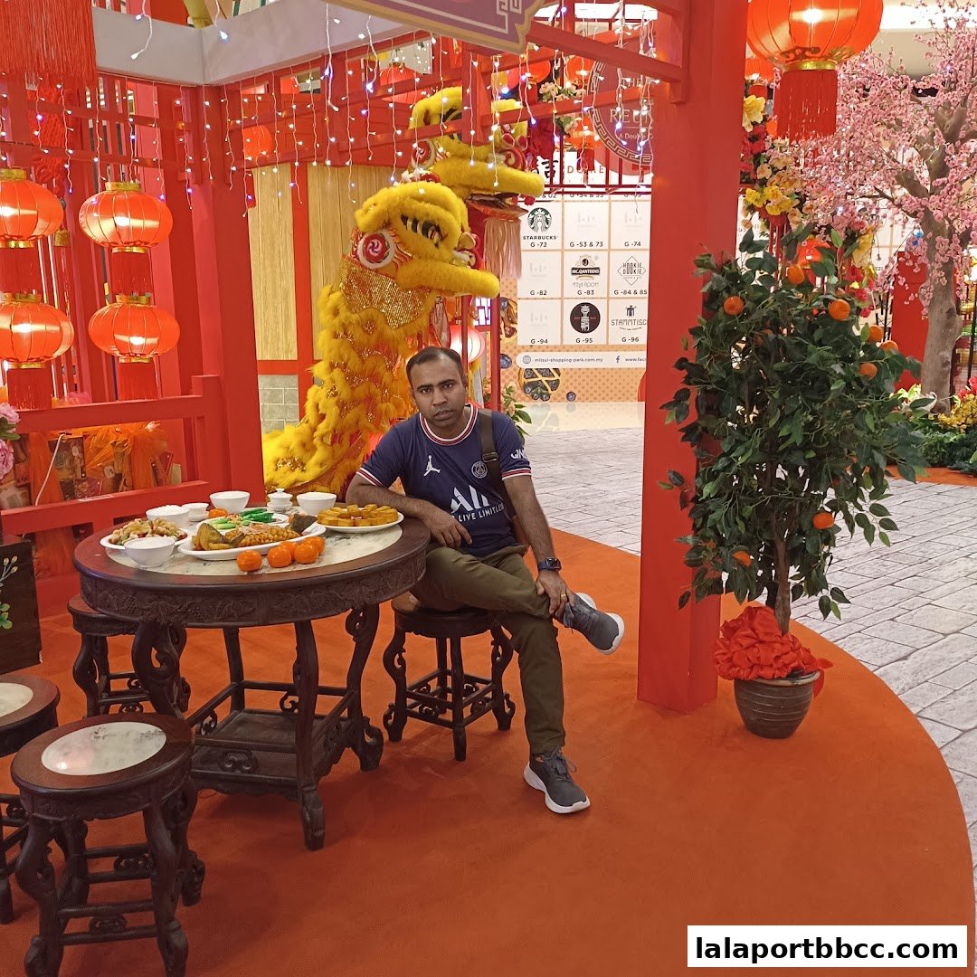 A man sits at a table with food, near a lion dance prop and festive decorations.