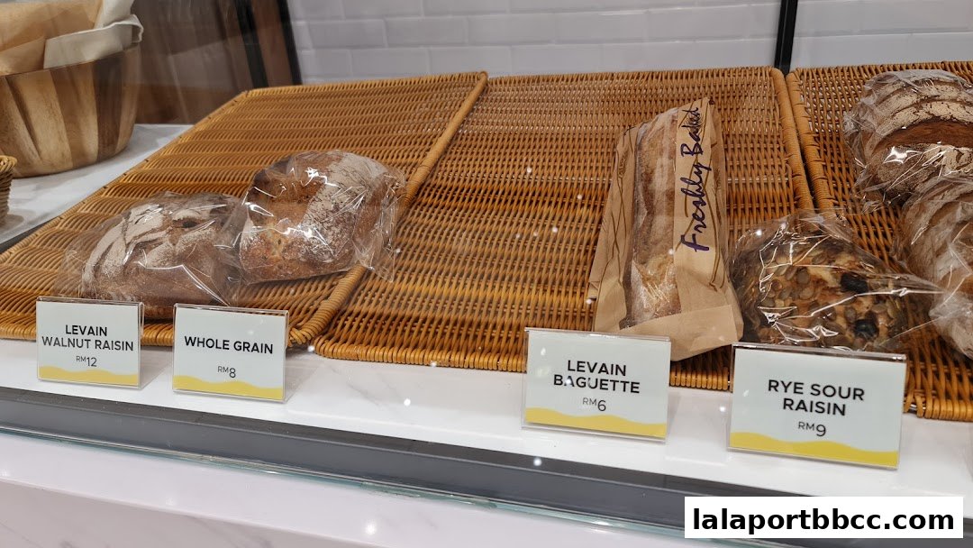 A display of freshly baked artisan breads, including Levain Walnut Raisin, Whole Grain, Levain Baguette, and Rye Sour Raisin.