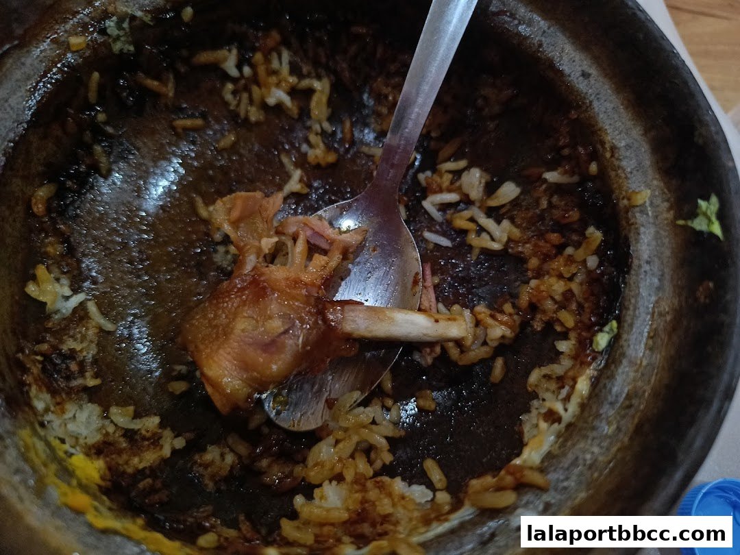 A close-up of a nearly empty claypot with leftover rice and chicken bones.