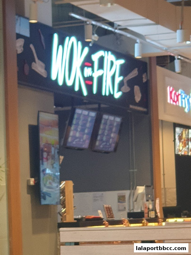 The brightly lit 'Wok On Fire' sign above a food counter with digital menus.