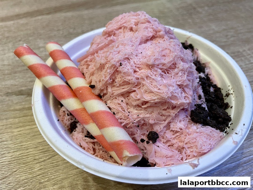A close-up of a pink shaved ice dessert with cookie crumbles and wafer sticks.