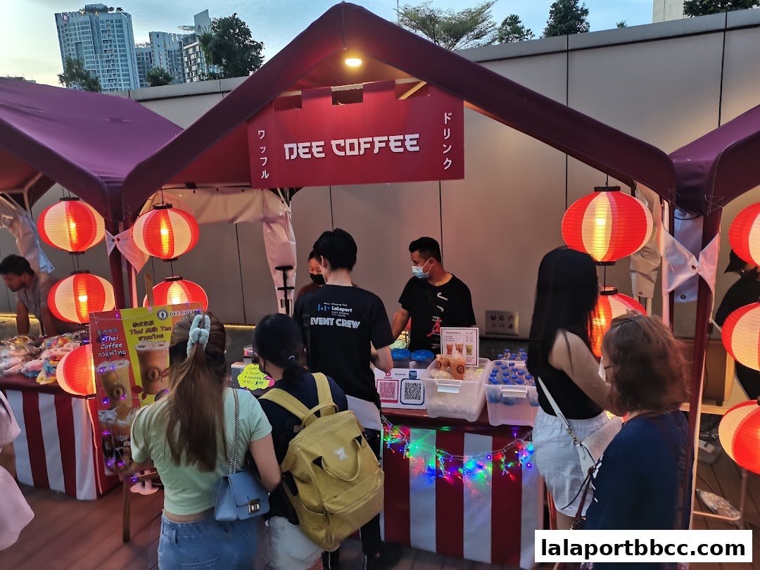 A busy outdoor stall named Dee Coffee Malaysia, decorated with red lanterns and fairy lights.