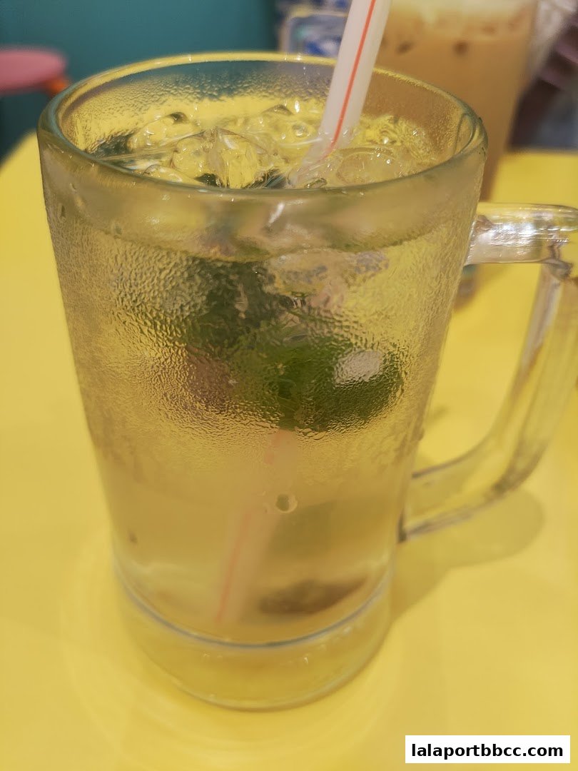 A close-up of a refreshing drink with ice and lime in a glass mug.
