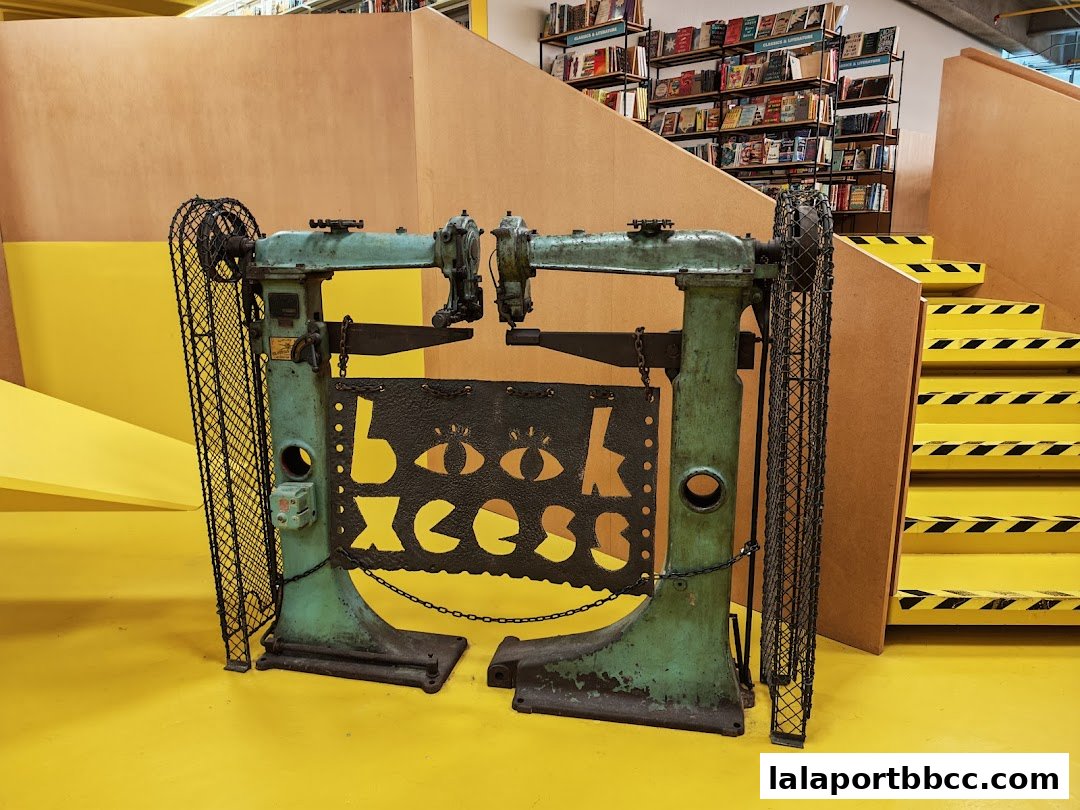 A vintage machine with the BookXcess logo in front of bookshelves and yellow stairs.