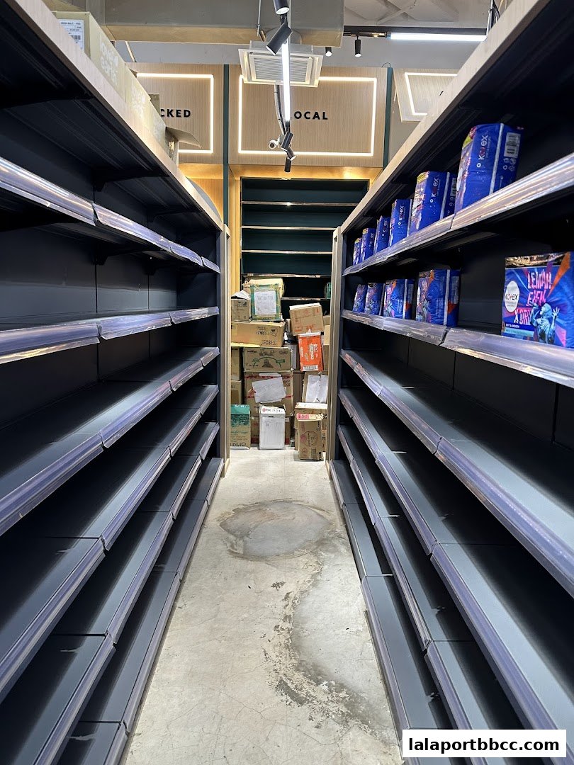 Aisle in a grocery store with empty shelves and some boxes stacked at the back.