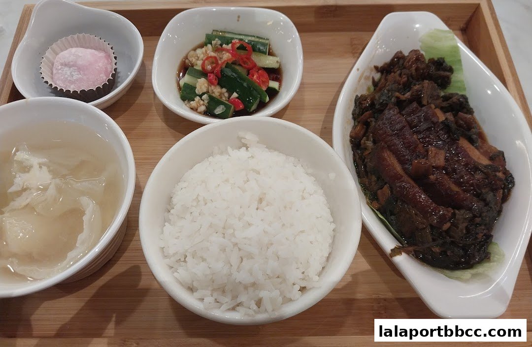A close-up of a delicious meal set with rice, soup, pickled cucumbers, braised meat, and a dessert.