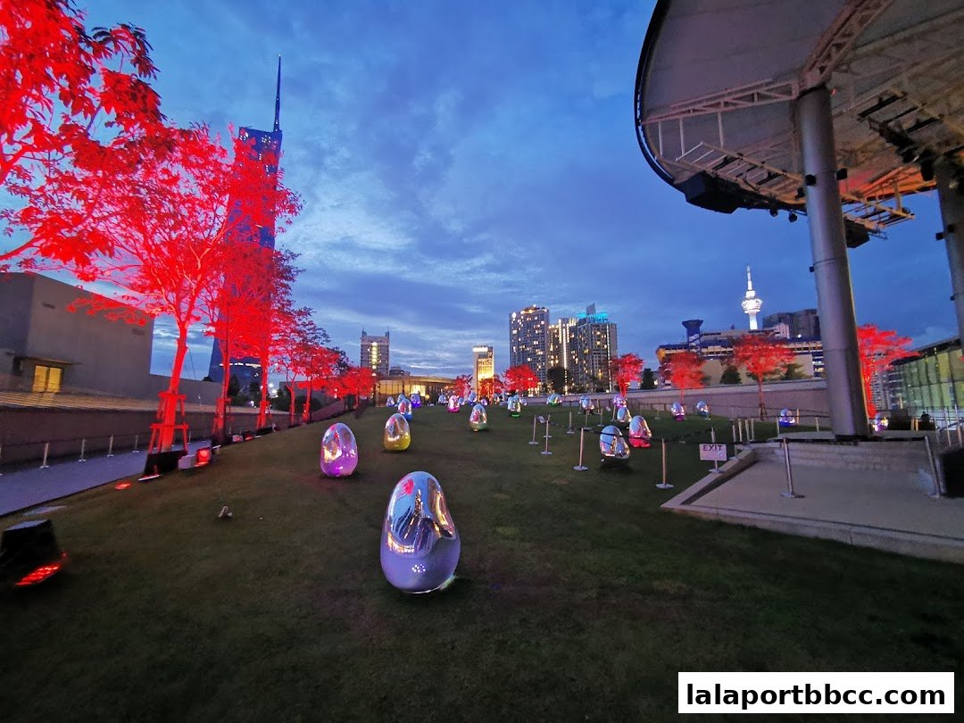 A rooftop garden with illuminated trees and egg-shaped sculptures at dusk.