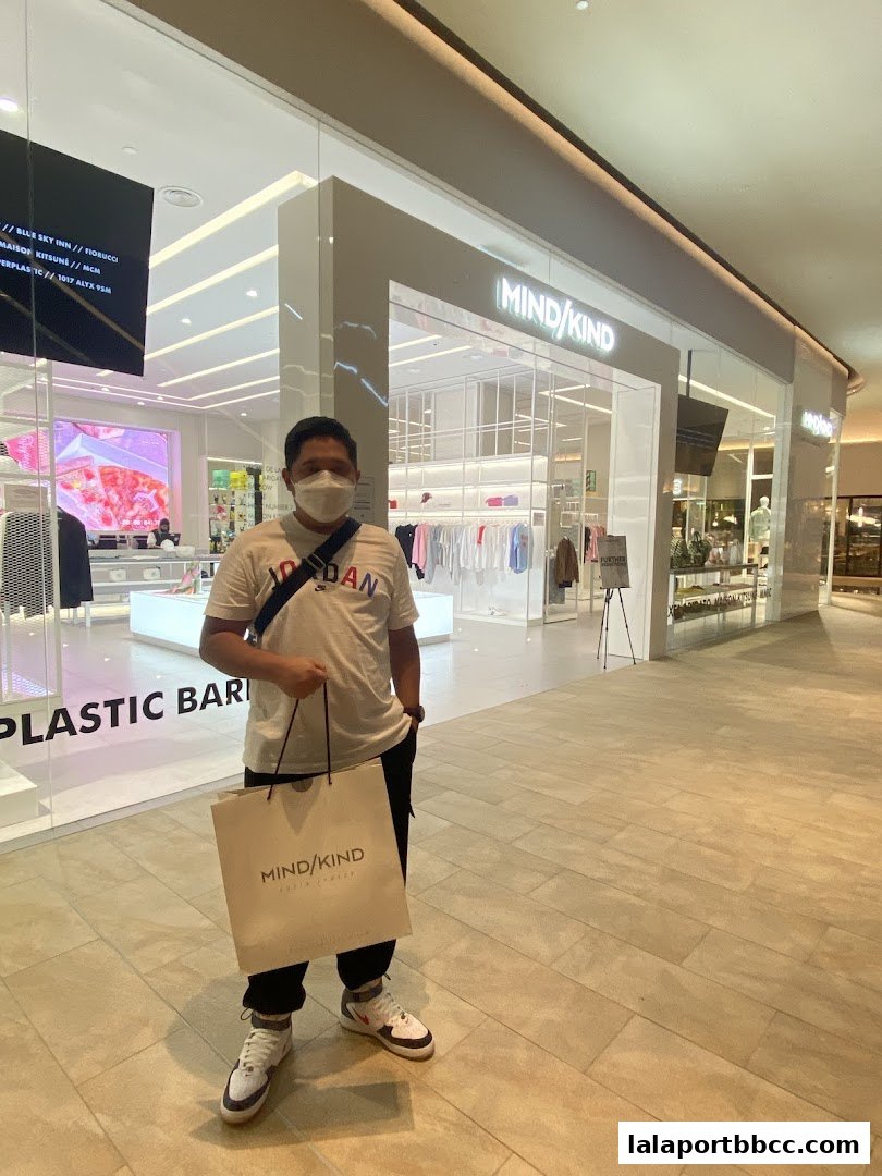 A person stands in front of the MIND/KIND store holding a shopping bag.