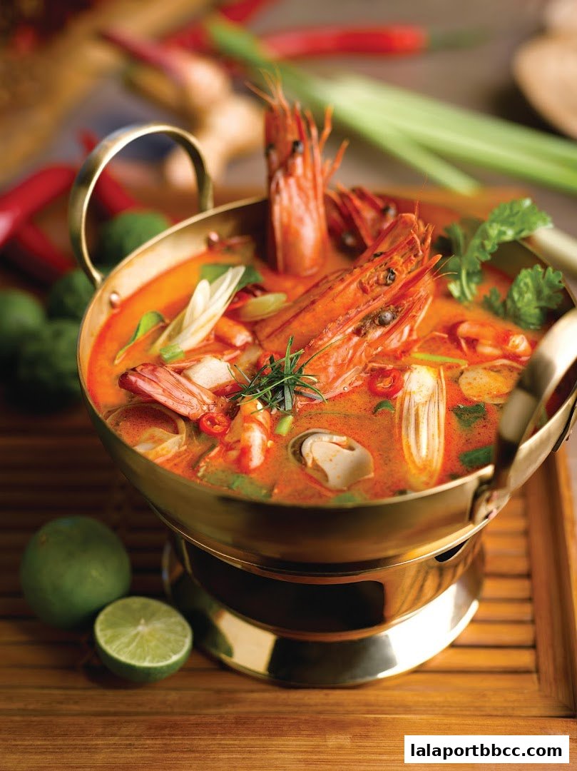 A steaming bowl of Tom Yum Goong soup with large prawns and fresh ingredients.