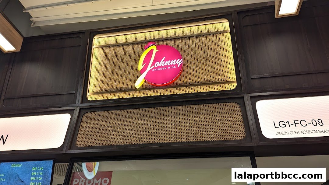 The illuminated logo of Johnny Chicken Rice is displayed on a dark wood panel wall.