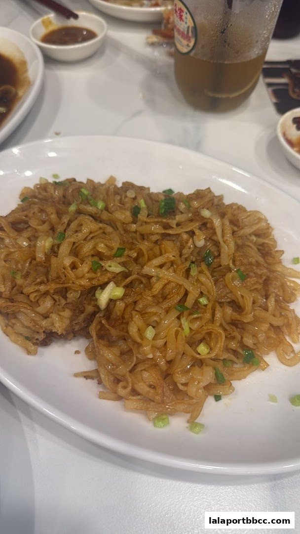 A plate of stir-fried noodles with chopped green onions and a side of dipping sauce.