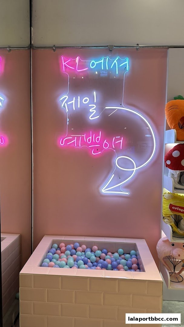 A pink wall with neon signs and a ball pit filled with pastel-colored balls.