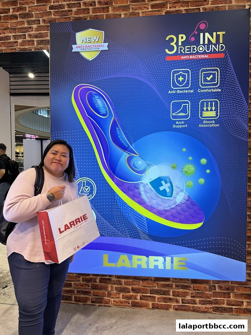 A woman holds a Larrie shopping bag in front of a large advertisement for Larrie shoes.