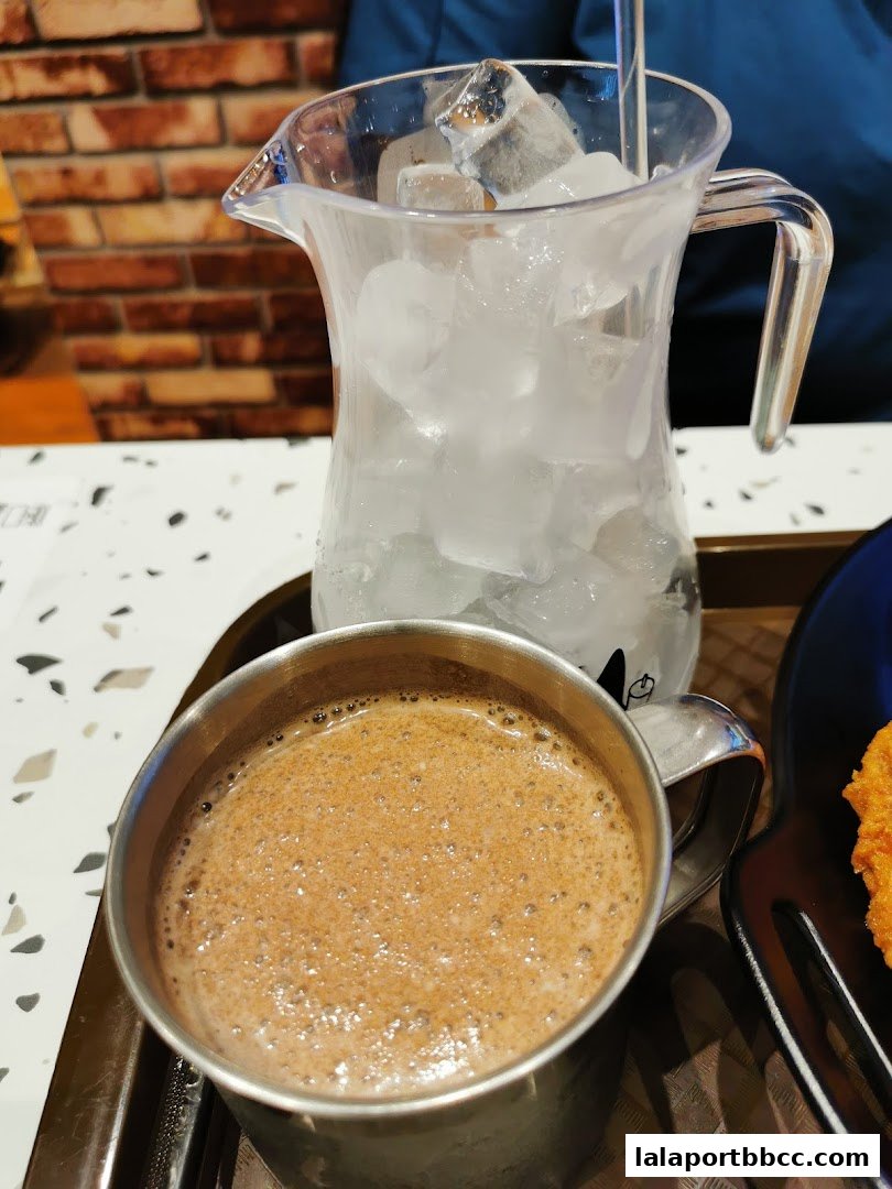 A close-up of a frothy hot chocolate served with a pitcher of ice water.