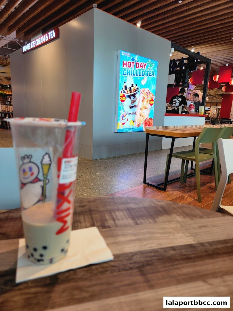 A bubble tea drink sits on a table in front of a MIXUE Ice Cream & Tea shop.