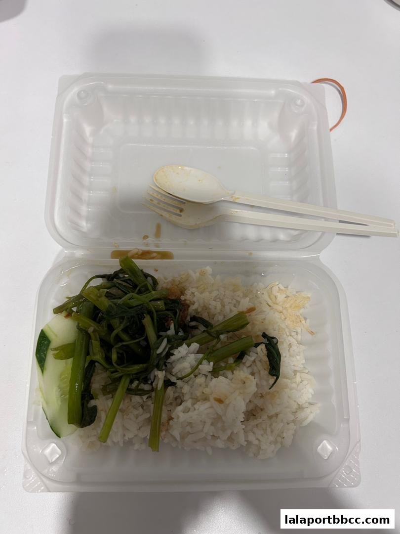 A takeaway container with rice, stir-fried vegetables, and cucumber slices, with used cutlery.