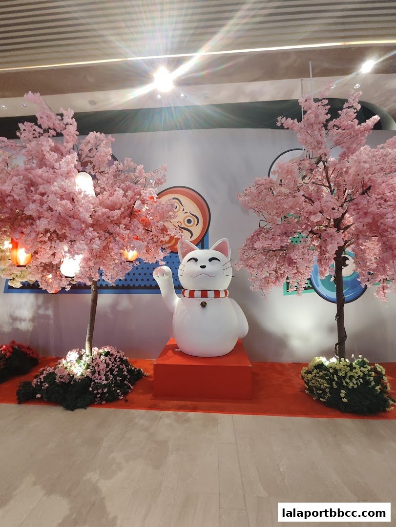 A festive display featuring a large Maneki-neko cat statue and cherry blossom trees.
