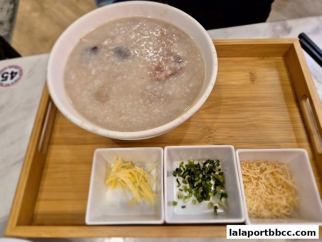 A bowl of congee with three small dishes of toppings on a wooden tray.