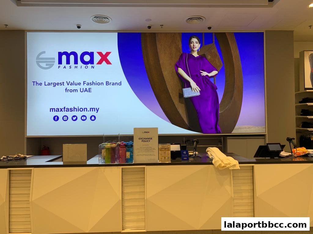 A large screen displays the Max Fashion logo and a model in a purple dress.