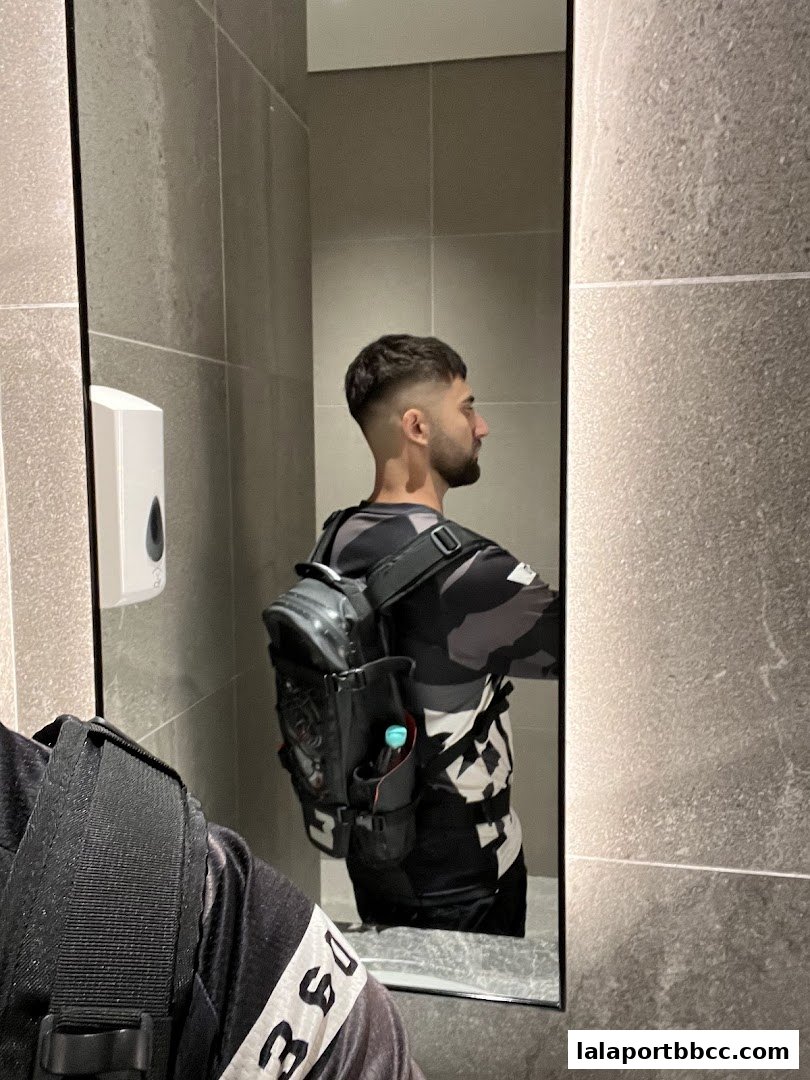A man with a fresh fade haircut and a backpack stands in front of a mirror.