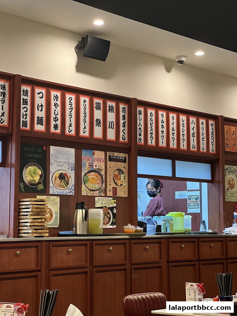 Interior view of a ramen shop with Japanese menu items displayed and a staff member behind the counter.